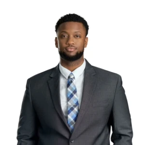 Professional man in dark suit and plaid tie standing against white background.